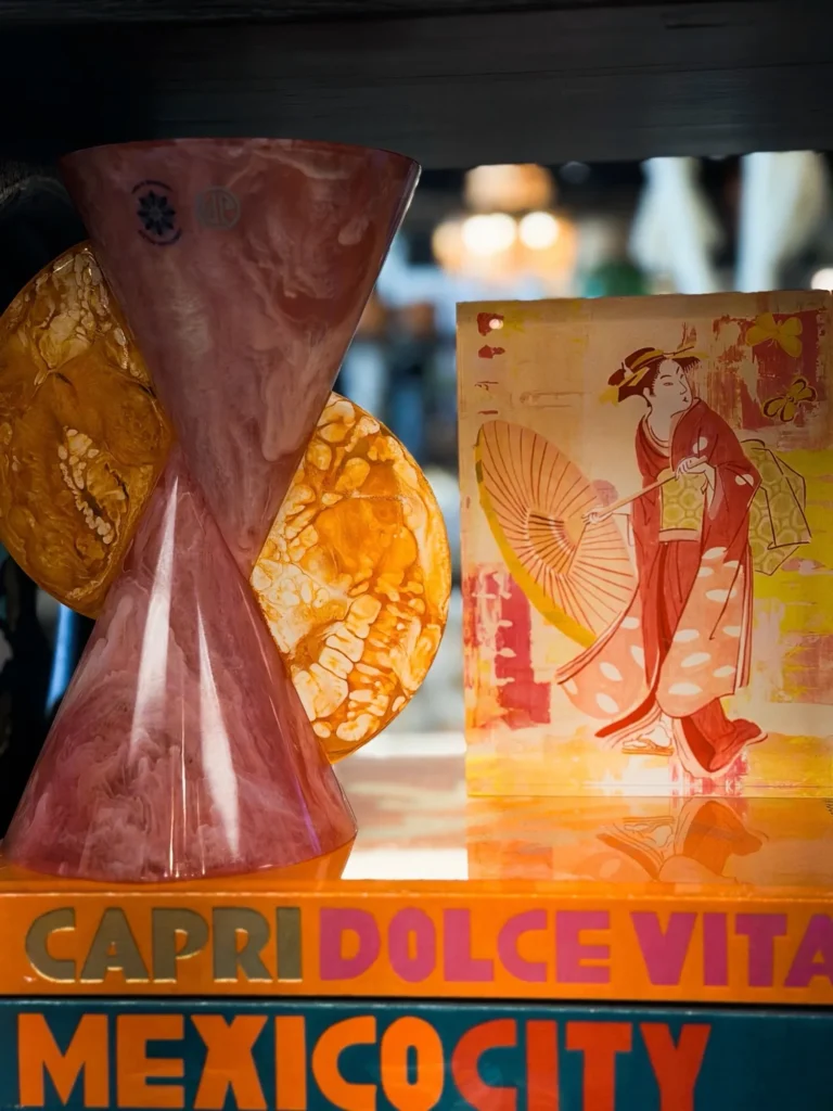 Pink glass vase and colorful art prints on a shelf